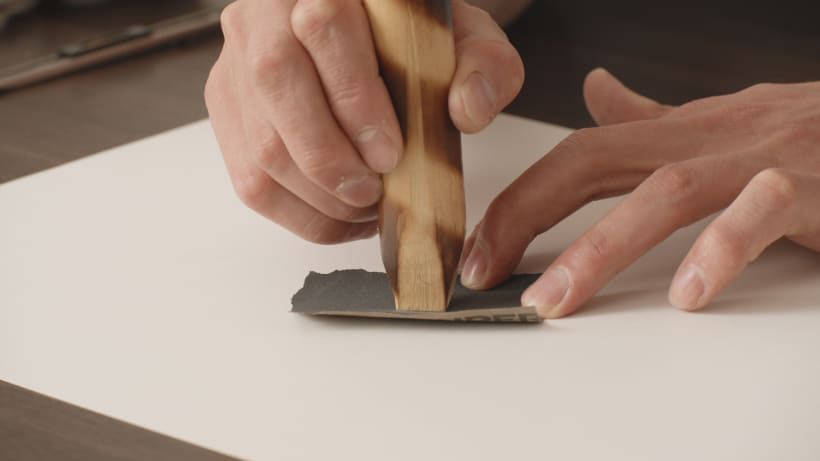 We sand the tip by resting the sandpaper on the table.