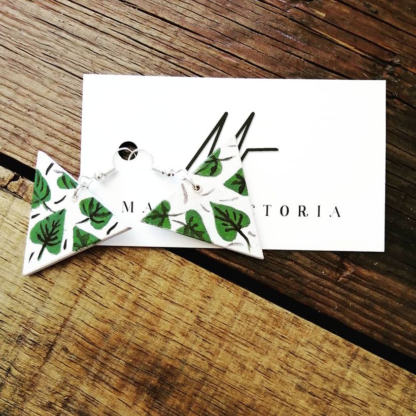 Aretes de madera en forma de triangulo con hojas pintadas.