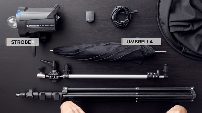 An umbrella directs the strobe light mounted on a tripod.