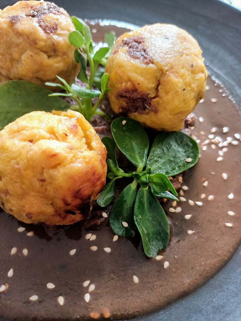 Tortitas de plátano macho rellenas de frijol en mole