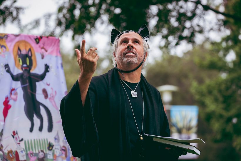 Giving eulogy of Blackie the Cat, wearing special costume, with Ascension painting banner in background. Photo by the1point8