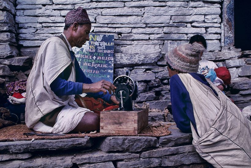 Um alfaiate faz reparos e produz roupas no terraço diante de sua casa.