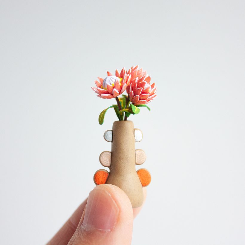 A tiny vase made from polymer clay with a few tiny stems of peeking out the top.