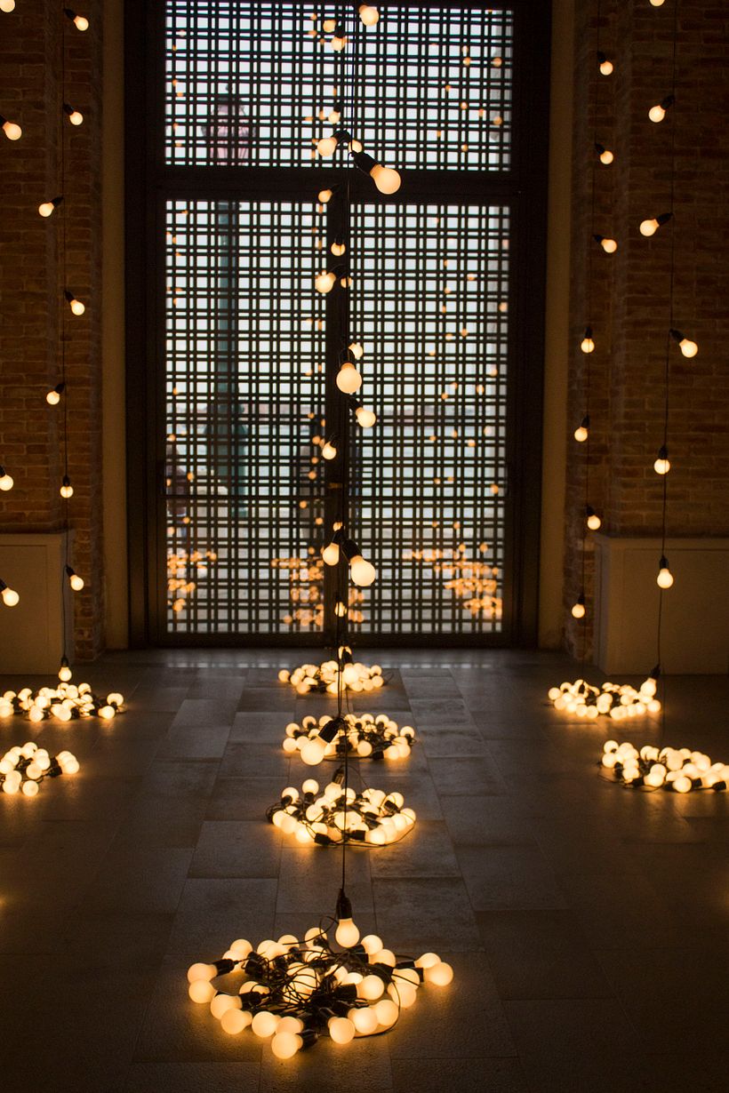 (Venice, 2019) The warm orange-yellow lights are cast on a string and hung from the ceiling, pooling into a bed of lightbulbs