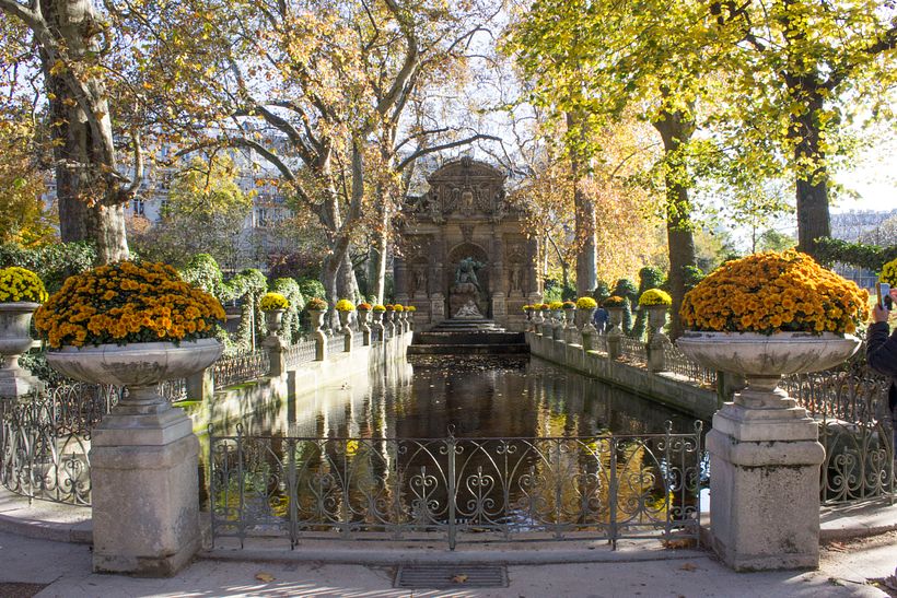 (Paris, 2019) A view of a parisian fountain, framed by the orange and yellow flowers and leaves of the overhead canopy.