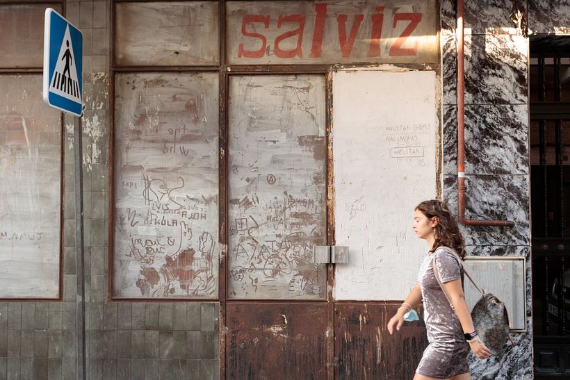 Mujer andando delante de la fachada de un comercio cerrado. Calle de San Amado.