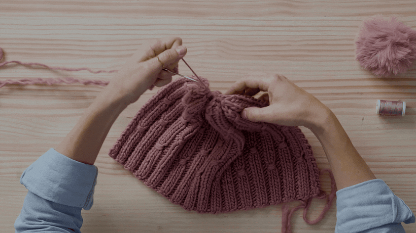 Con costura invisible, une los extremos de la tela y añade un pompón como toque final.