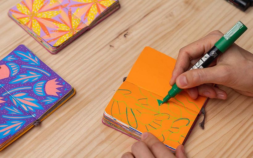 Polina travaille sur une feuille de papier orange insérée et découpée dans son carnet de croquis.