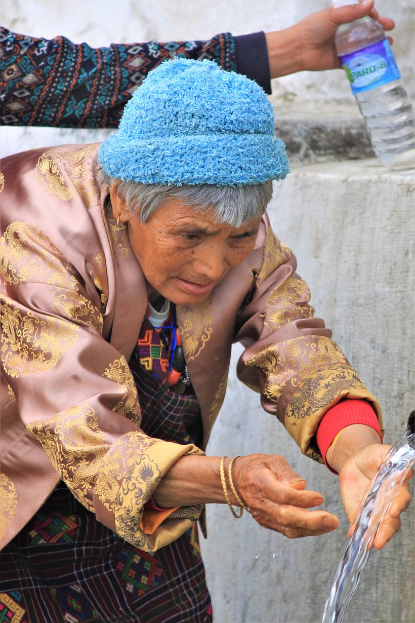 A woman soaks her hands and face in Tshrim Drupchhu, a holy water spring which is said to purify negative deeds.