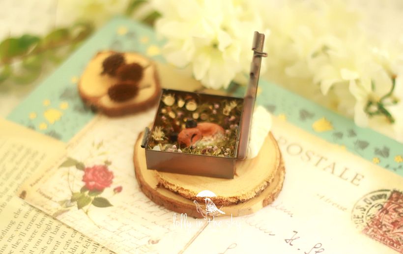 pingente de metal com tampa de vidro. Em seu interior, a raposinha em polymer clay dorme entre pequenas flores preservadas