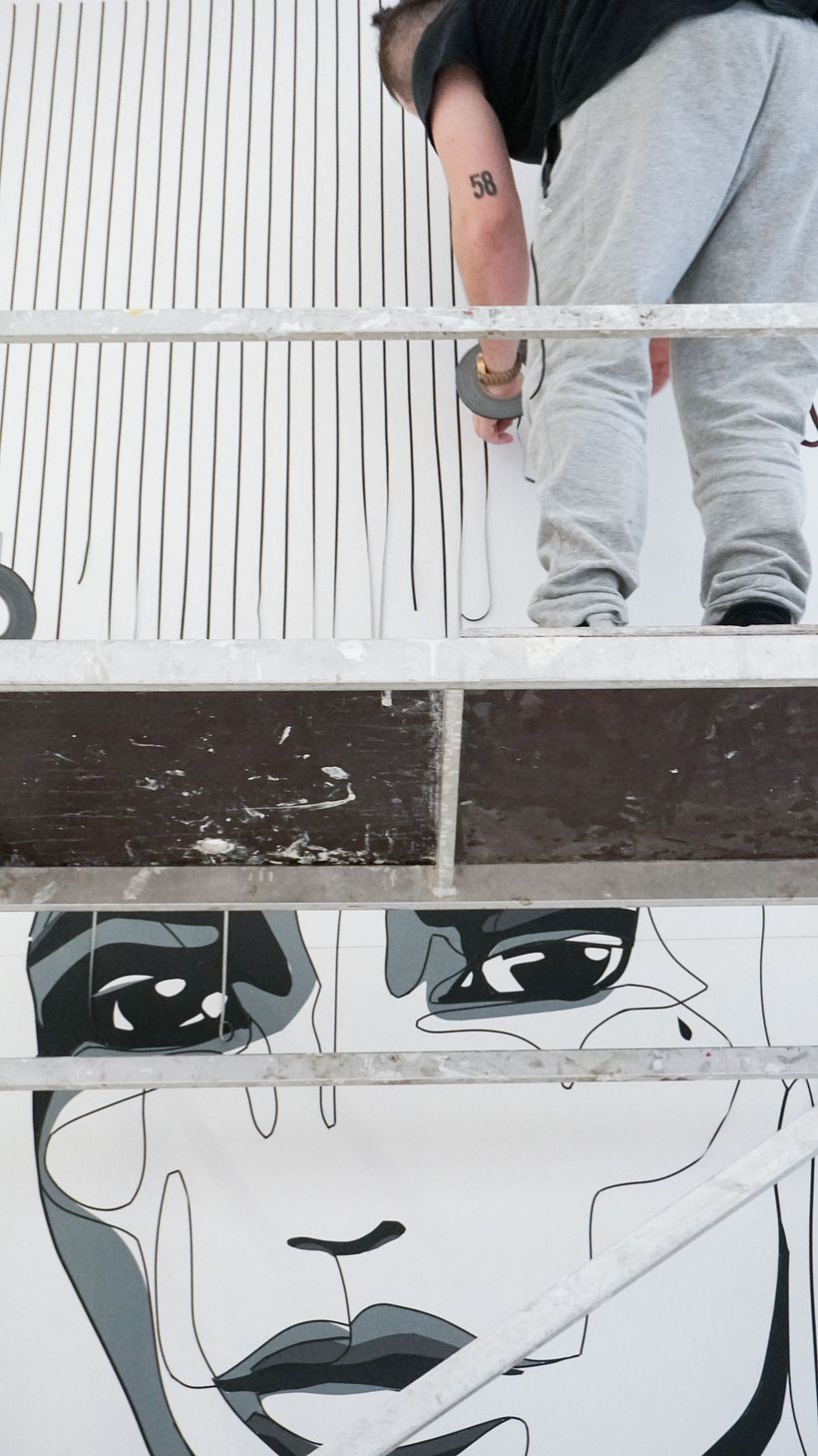 Nicolas Lawin taping a portrait-mural