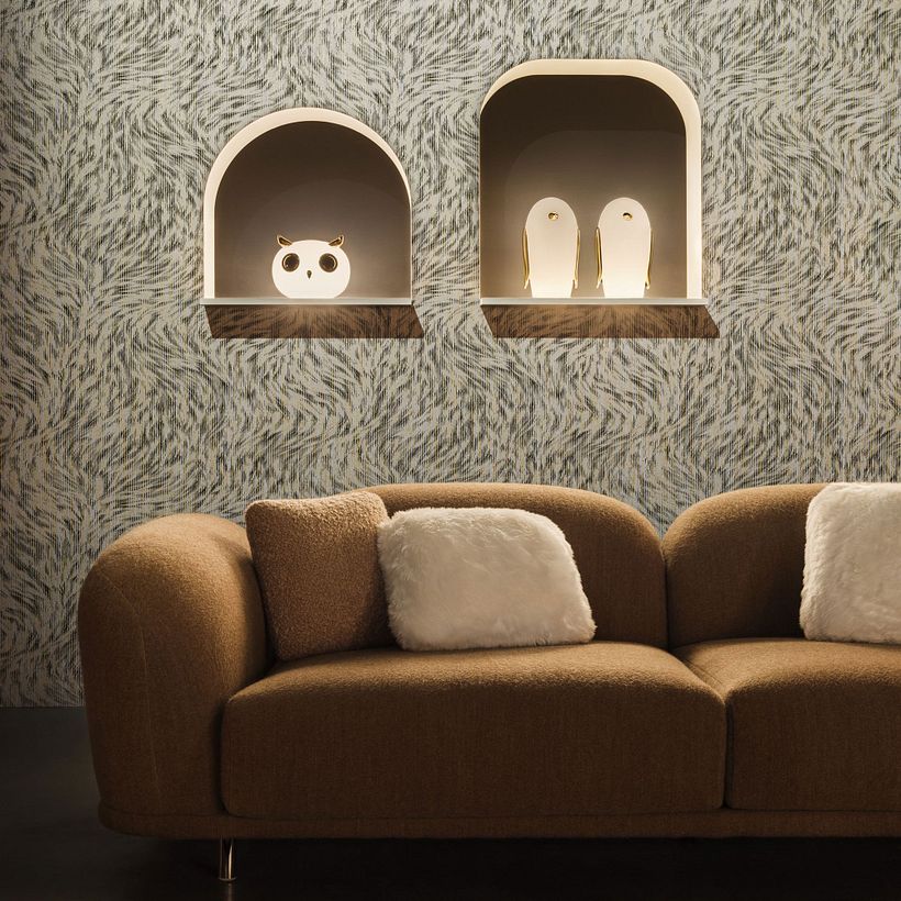 A sofa with fluffy pillow is placed in front of two small arches containing 2 bird shaped lamps.