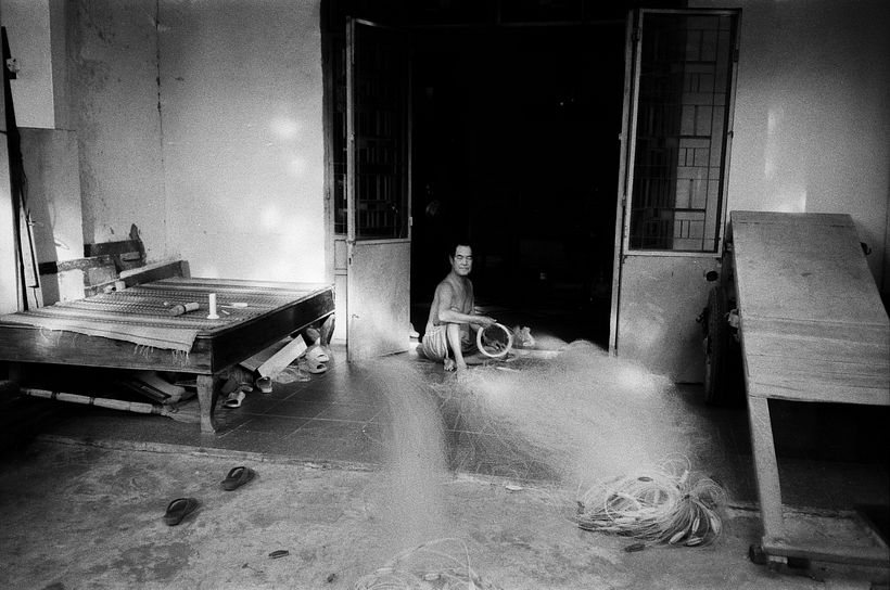 Un viejo pescador remendando sus redes en su casa en el barrio de Man Thai.