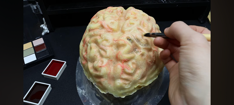 Putting cosmetic onto the fake latex brain for this look.