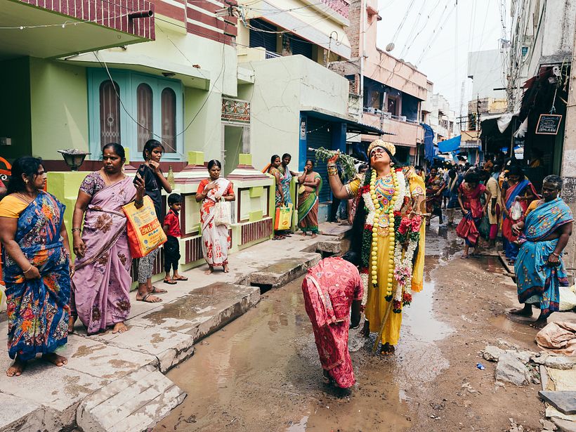 A man in the disguise of godess Parvathi in trance walks in the street and people comfort her by pouring water on her feet